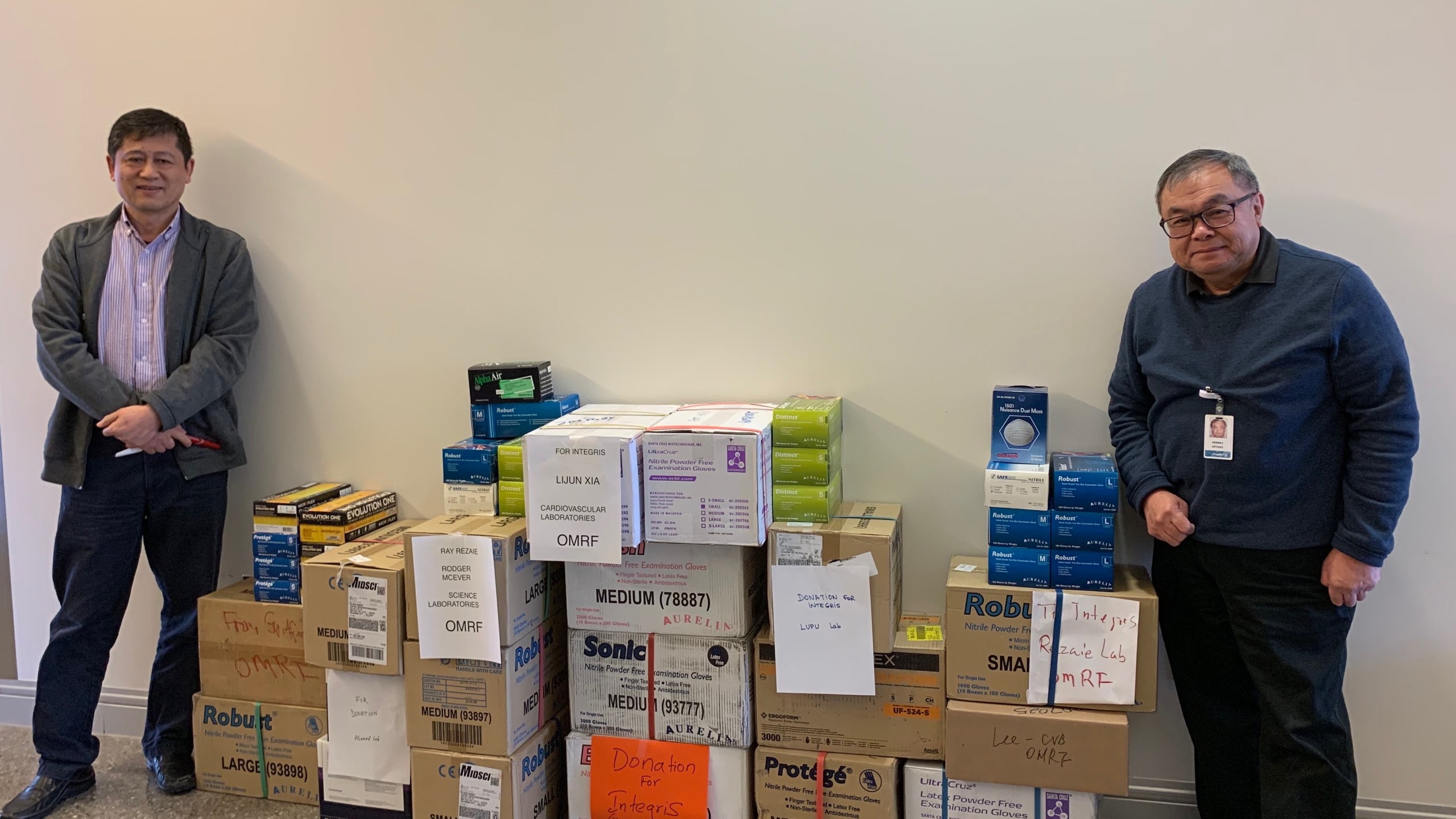 Lijun Xia, M.D., Ph.D., and Hendra Setiadi, Ph.D., with the laboratory gloves the Oklahoma Medical Research Foundation donated to Integris Baptist Medical Center for use during the COVID-19 coronavirus pandemic. March 2020